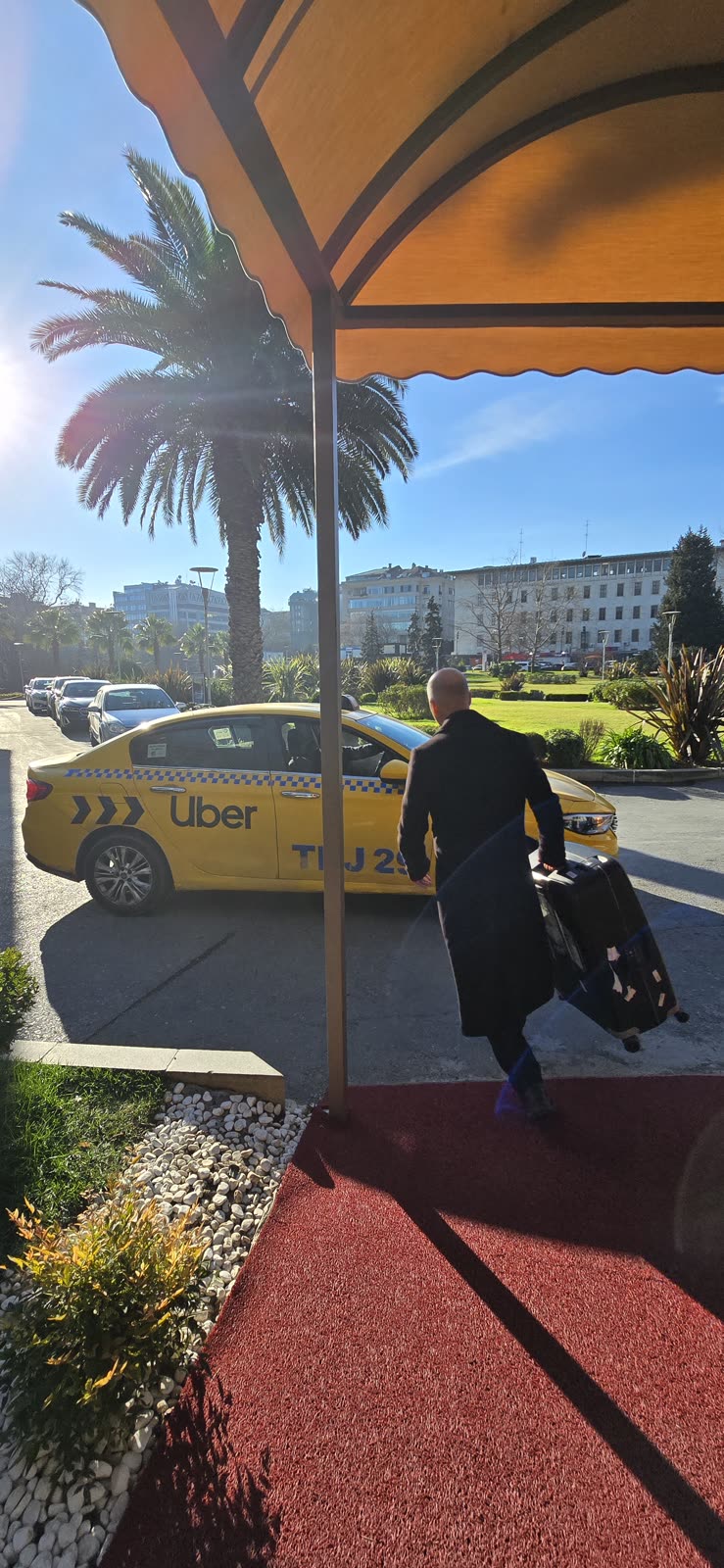 man walking with a rolling suitcase past a yellow uber taxi at a hotel entrance