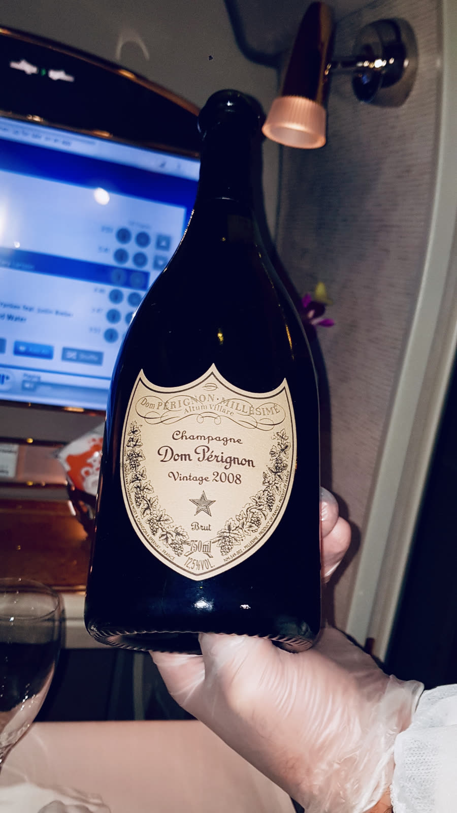 hand holding a bottle of Dom Perignon champagne inside an airplane first class cabin